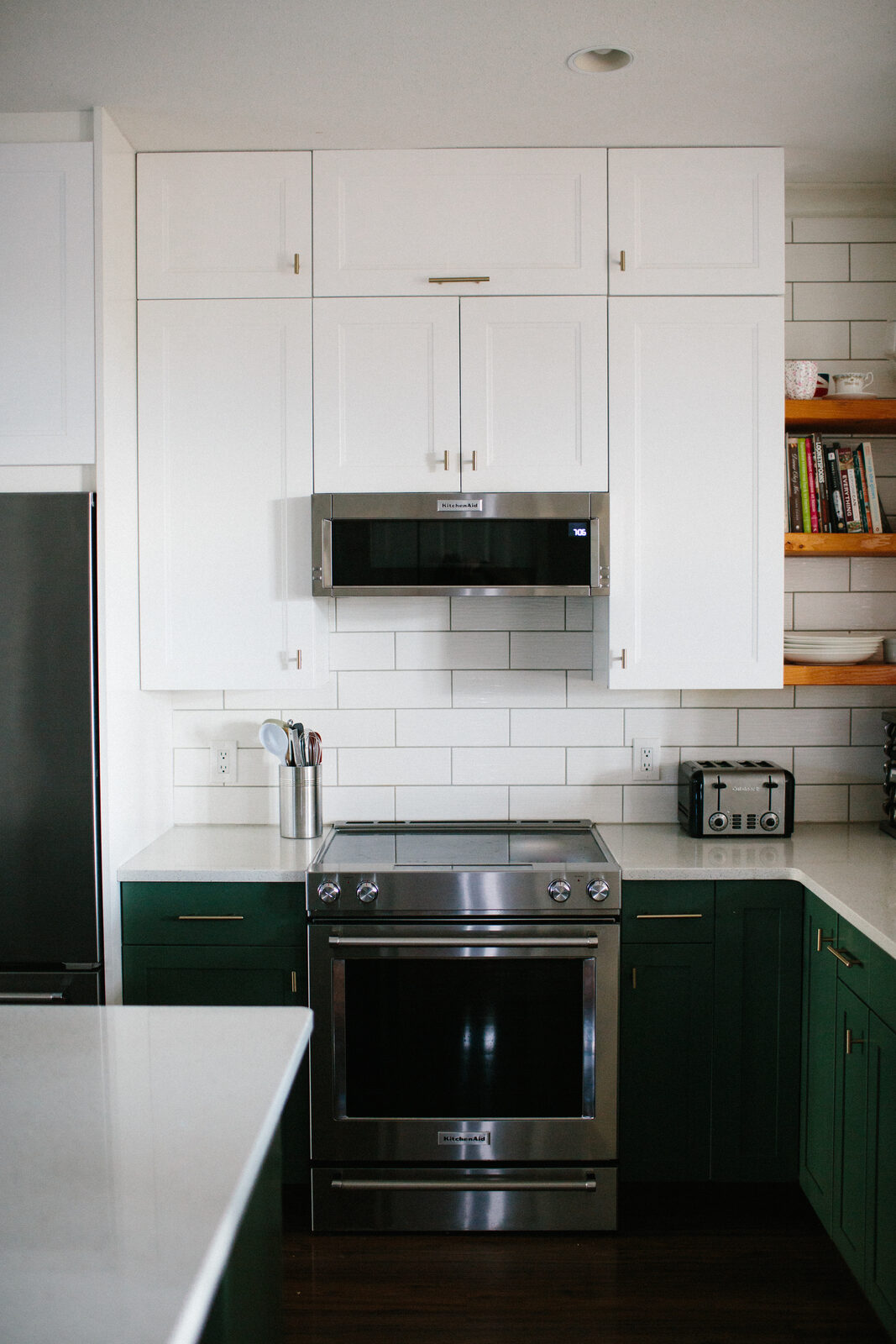 White shaker upper cabinets stacked to the ceiling above deep green base cabinets and a white subway tile backsplash