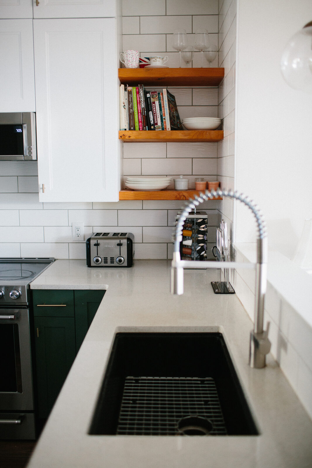 Floating stained-wood shelves against a full-height white subway tile backsplash above green base cabinets